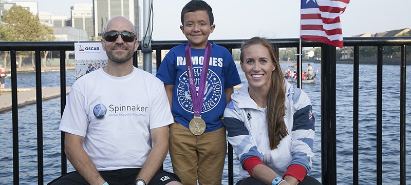 A little boy wearing a medal stands between a man and a woman outside.