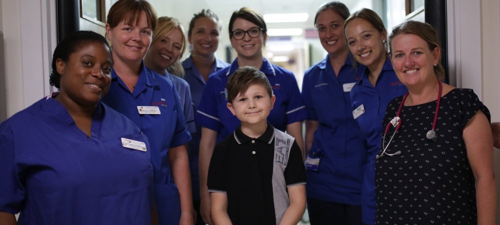 A young boy standing on a hopsital ward with staff