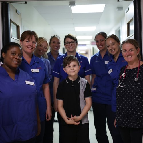 A young boy standing on a hopsital ward with staff