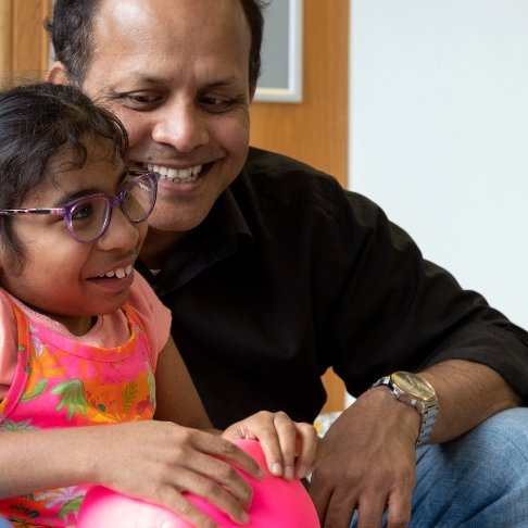 GOSH patient holds a balloon while sitting next to her dad, at GOSH. They are both smiling.