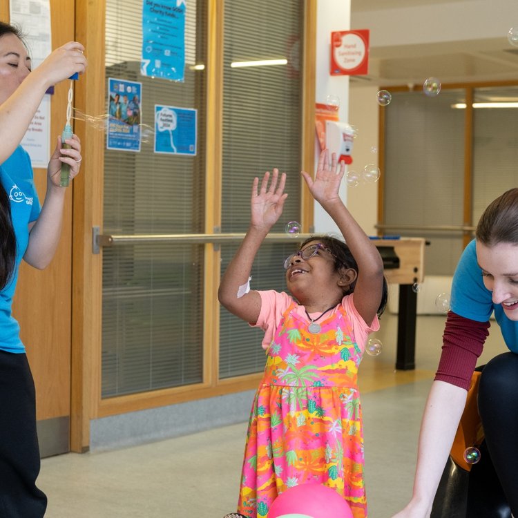 GOSH patient waves her hands in the air as a member of GOSH Arts blows bubbles