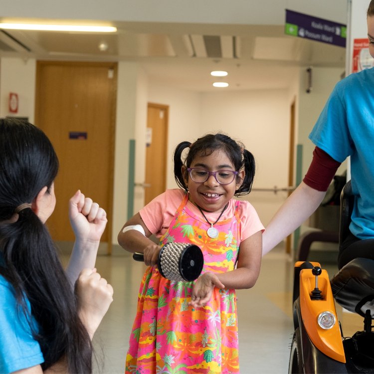 GOSH patient smiling and playing a percussion instrument while standing next to two members of staff at GOSH Arts