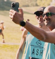 Two TeamGOSH London Marathon runners are taking a selfie before the beginning of they race. They have been captured by the TeamGOSH photographer. Both runners are wearing blue GOSH Charity vests, sunglasses and black shorts.