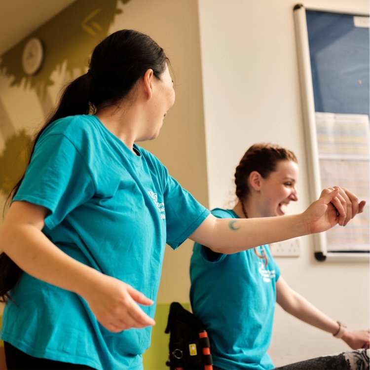 Two members of GOSH Arts smile and hold hands while performing.