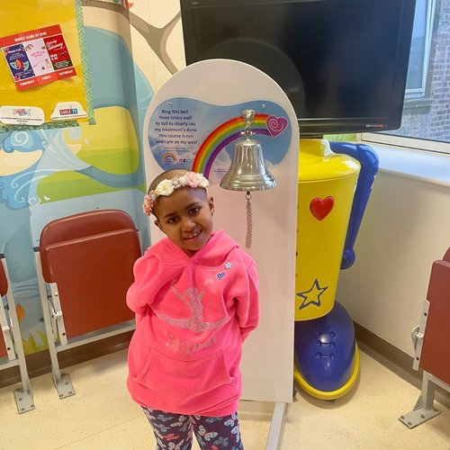 Girl stands next to end of treatment bell, smiling