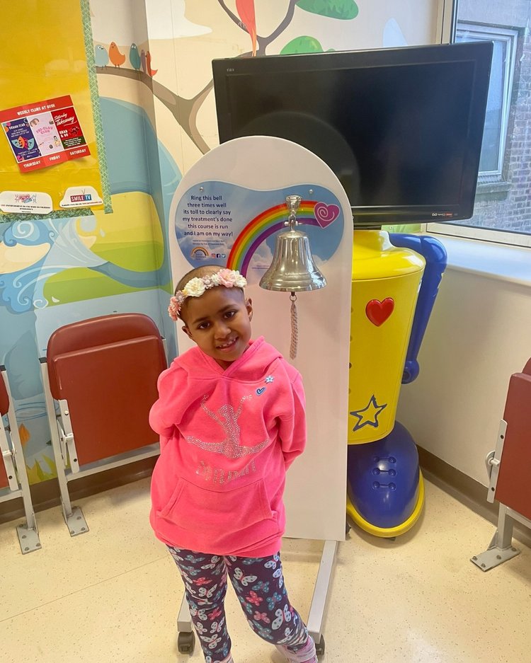 Girl stands next to end of treatment bell, smiling