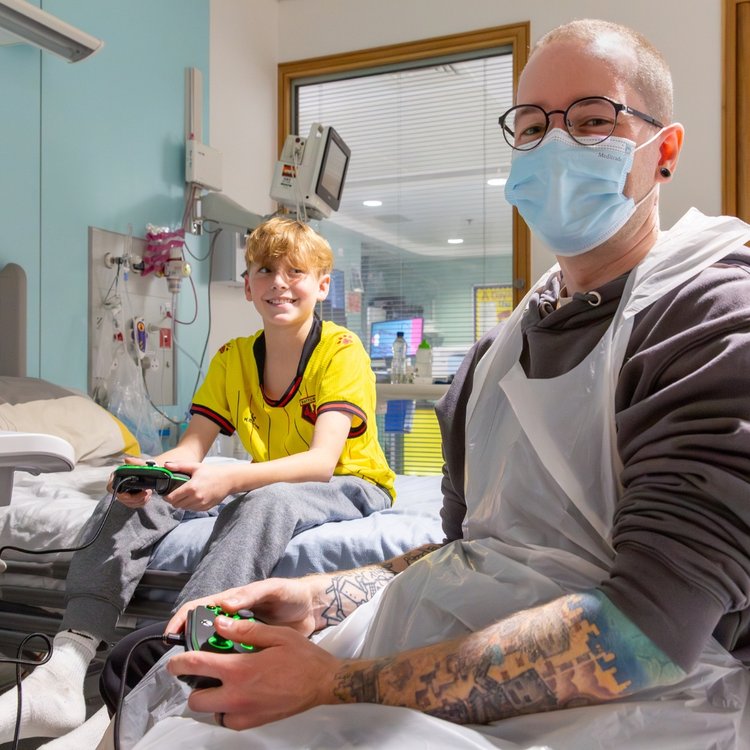 DanTDM, wearing a face mask, with patient, who is smiling, playing a game of FIFA.