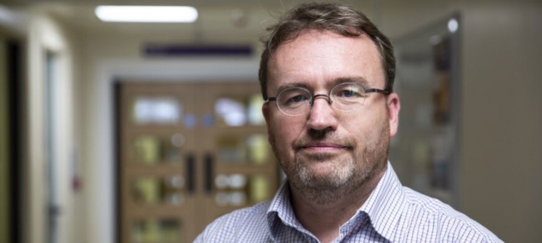 Headshot of Professor Darren Hargrave. He is standing in a hospital corridor and looking to camera.