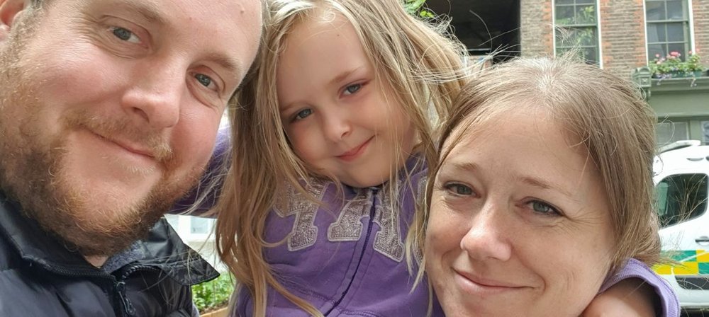 Zoomed in photo of Ellie outside, with her parents either side of her, smiling to camera
