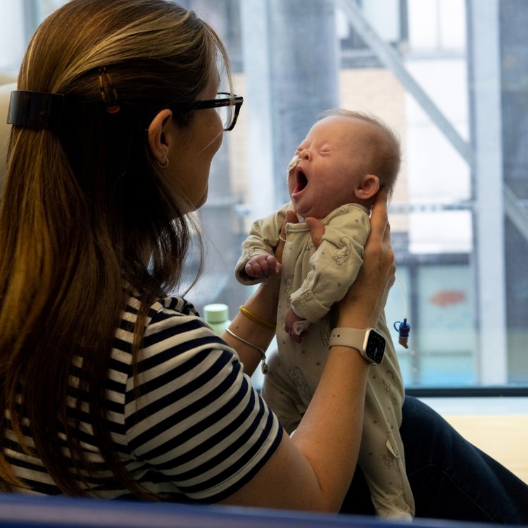 GOSH mum holds her baby daughter, so that she can stand upright on her lap. Baby is yawning.