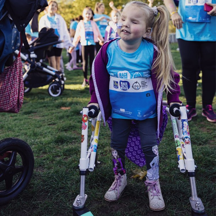 Photo of Emily at RBC Race for the Kids last year. She is standing outside holding her walker, smiling.