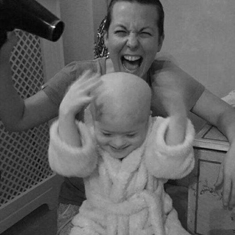 Black and white photo of little girl and her mum. Mum is holding a hair dryer and they are both smiling.
