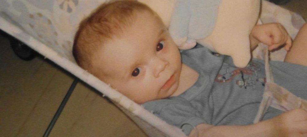 Photo of Jake as a baby, lying down in chair and looking to his side - at camera