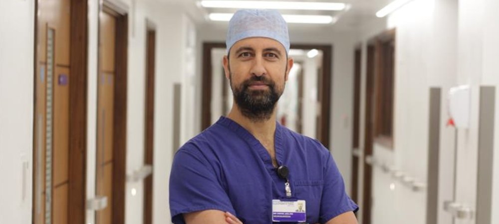Man wearing scrubs standing in corridor and looking to camera