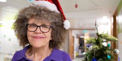 Lizzie smiling to camera while on the ward at GOSH. She's wearing a Christmas hat and standing next to a Christmas tree.