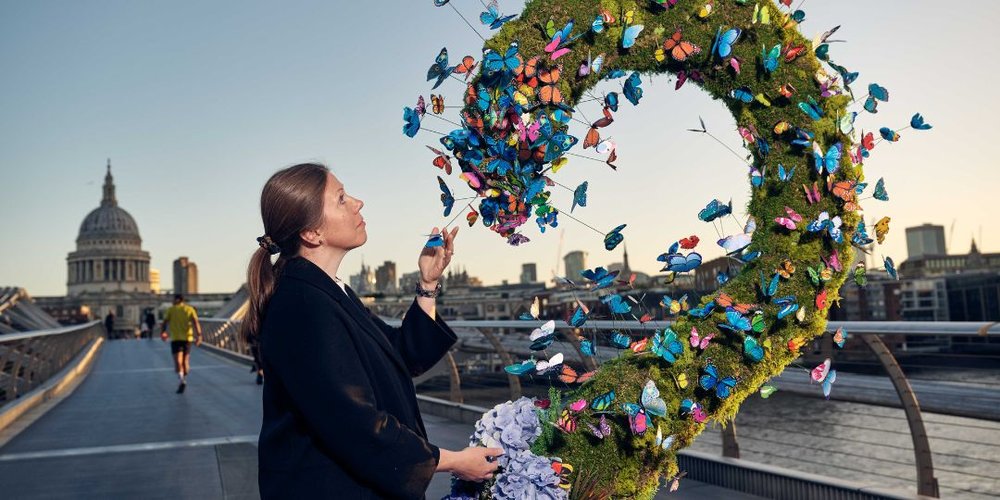 Woman in a coat observes butterfly installation on Millennium Bridge. St Paul's Cathedral can be seen in the distance
