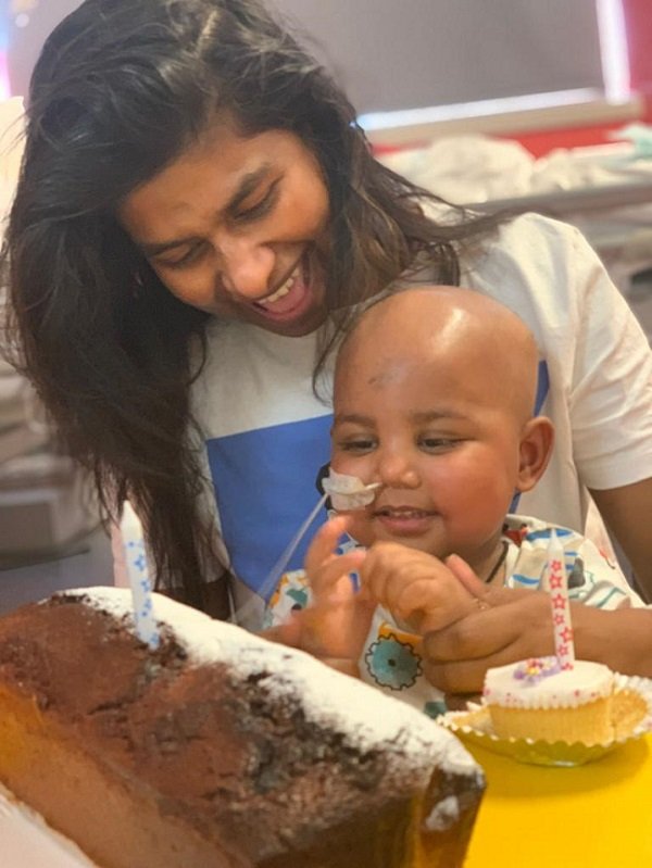 A little boy and his mother smiling looking at two cakes with candles on it
