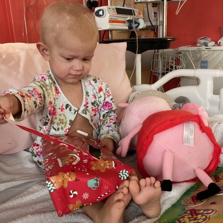 Patient Orla opening a Christmas present sitting on her hospital bed