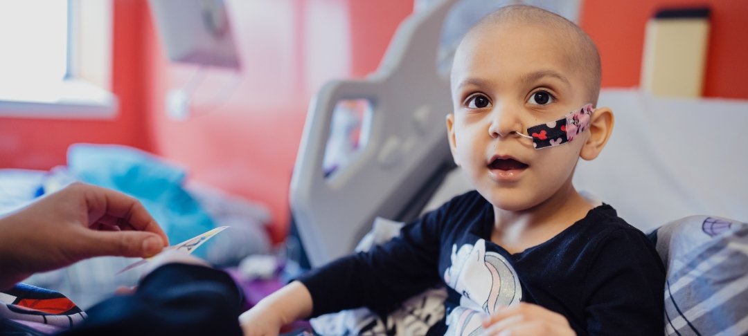 Girl with feeding tube sits in her room at GOSH. She is looking up and smiling.
