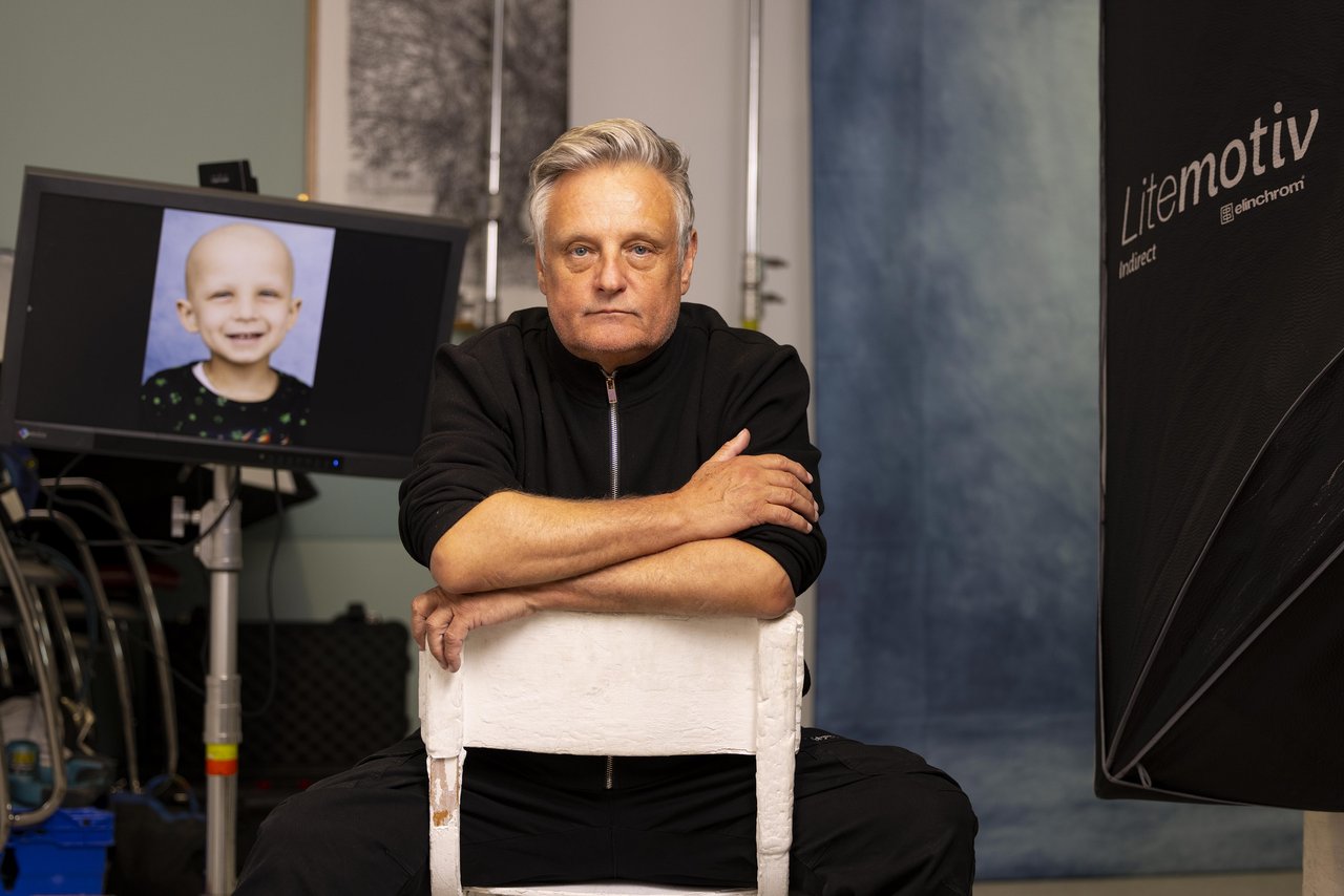 Photographer Rankin sits on a chair with his photos on a screen in the background