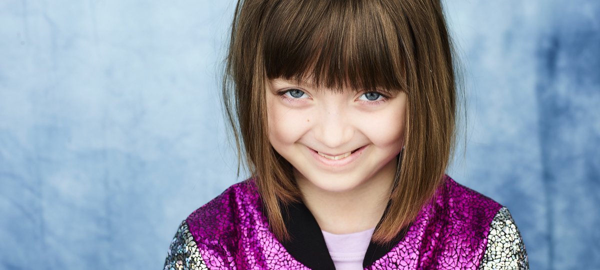 Portrait of GOSH patient Ellerie by photographer Rankin. Ellerie is wearing a sparkly purple and silver jacket and is smiling.