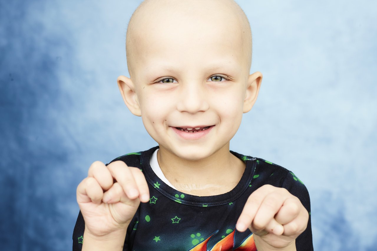 Portrait of GOSH patient Julian by photographer Rankin. Julian is wearing a black t-shirt with patterns on it. He's holding his hands up towards the camera.