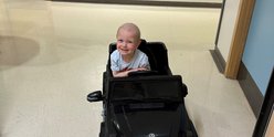 Hugo sitting in toy car in oncology ward. Smiling and looking to camera.