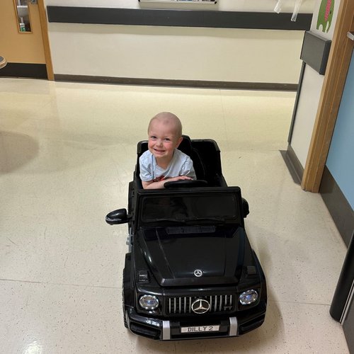 Hugo sitting in toy car in oncology ward. Smiling and looking to camera.