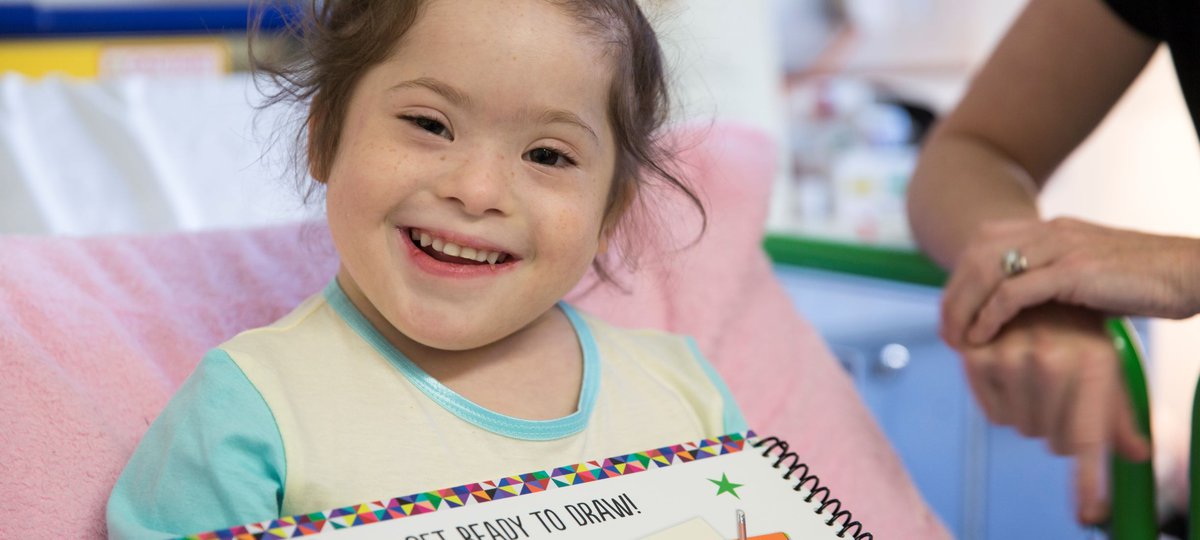 Patient Grace in a hospital bed holding a drawing book and smiling to camera