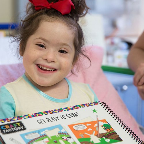 Patient Grace in a hospital bed holding a drawing book and smiling to camera