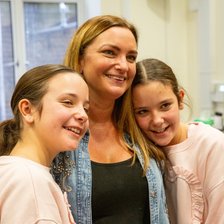 Twins Rosie and Ruby standing either side of their mum Angela, smiling.