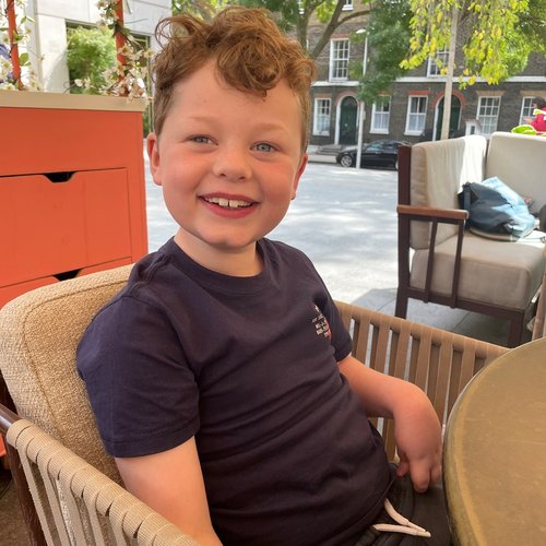 Sam is sitting in a wicker chair at a restaurant. He is smiling and looking at the camera.