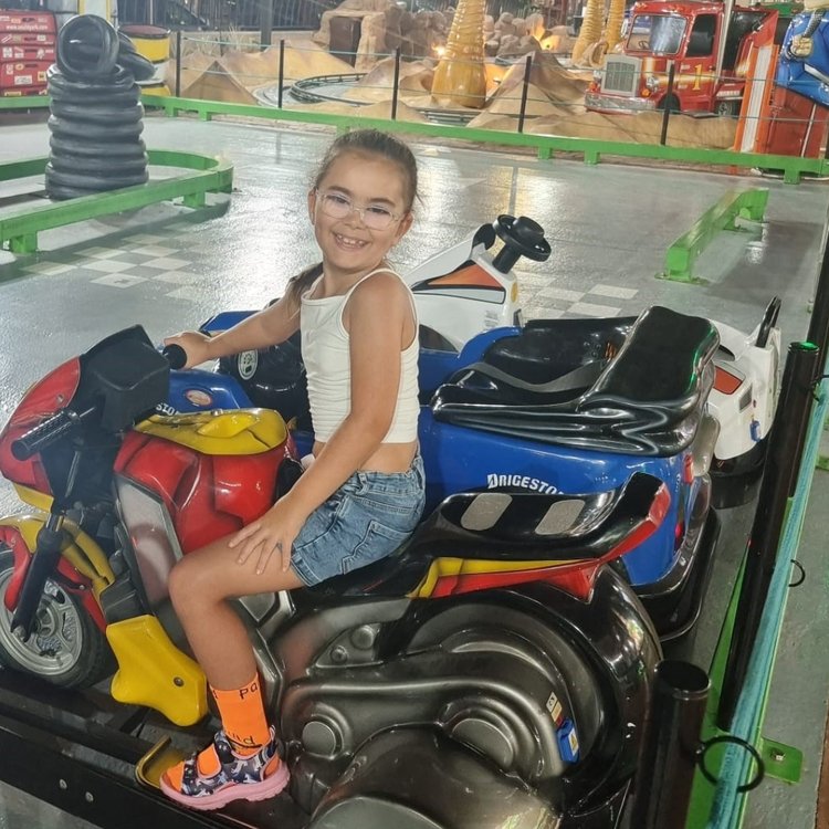 Girl looking to camera and smiling while sitting on toy motorbike in park