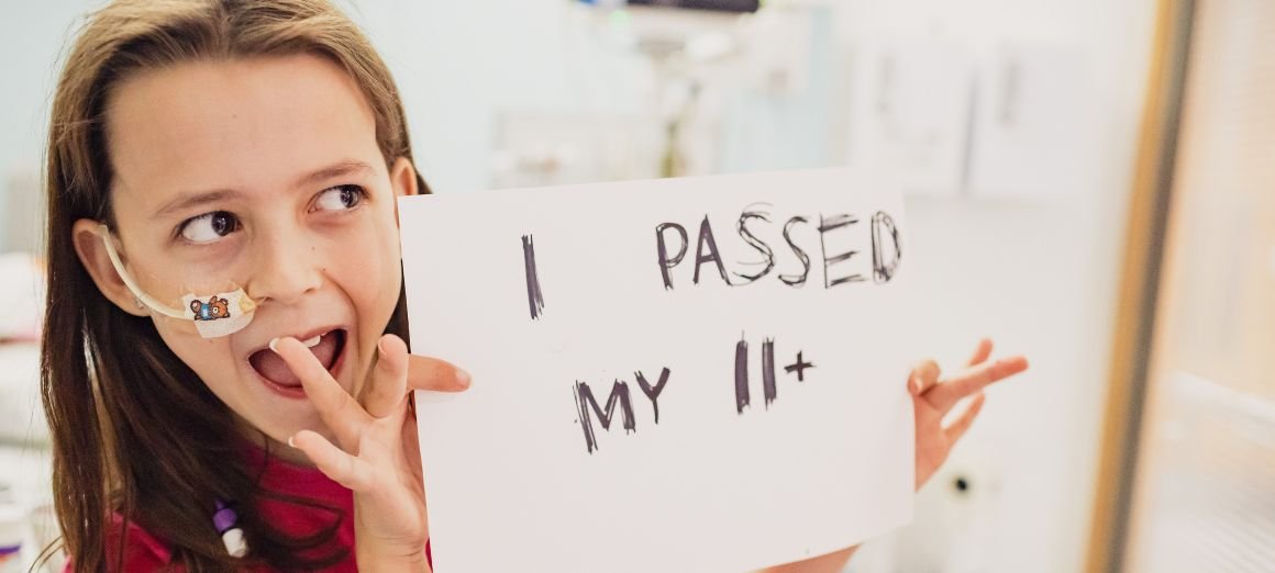 Photo of Sophia smiling and holding a sign reading "I passed my 11+".