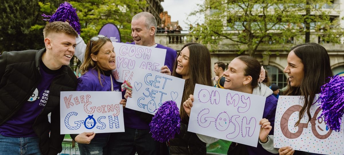 Group of people smiling and holding signs at GOSH Charity cheer point