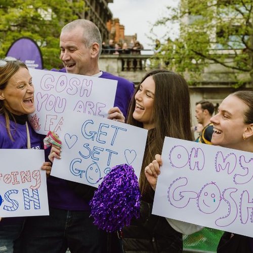Group of people smiling and holding signs at GOSH Charity cheer point