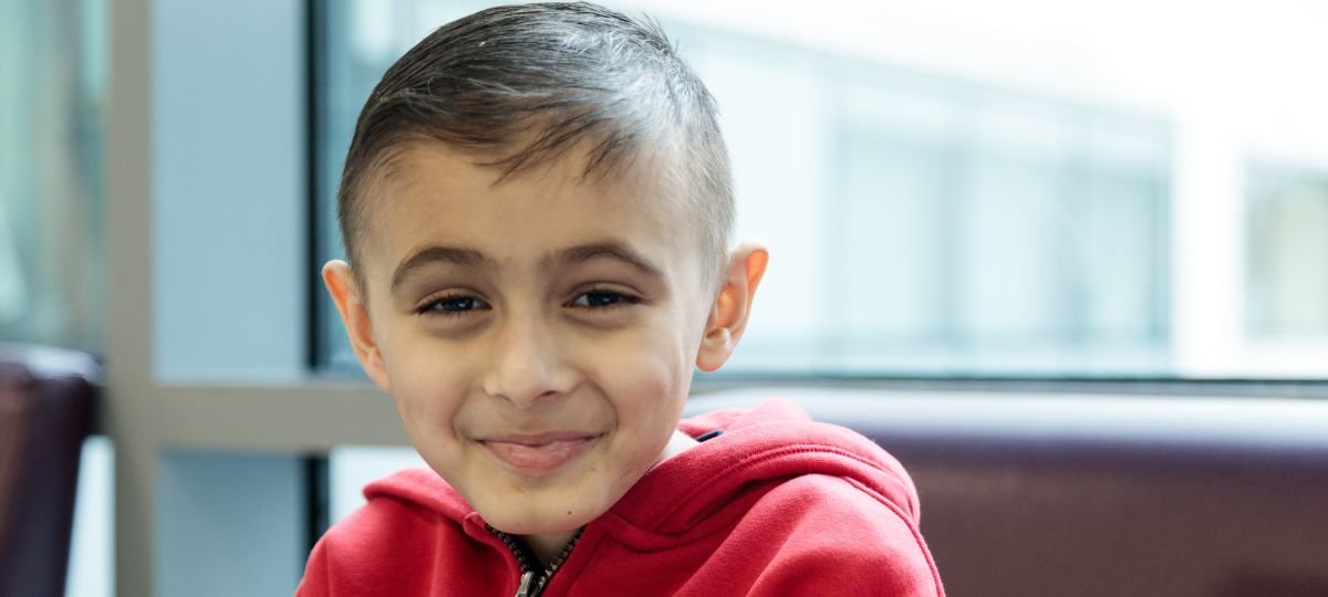 Headshot of boy wearing red hoodie smiling to camera.