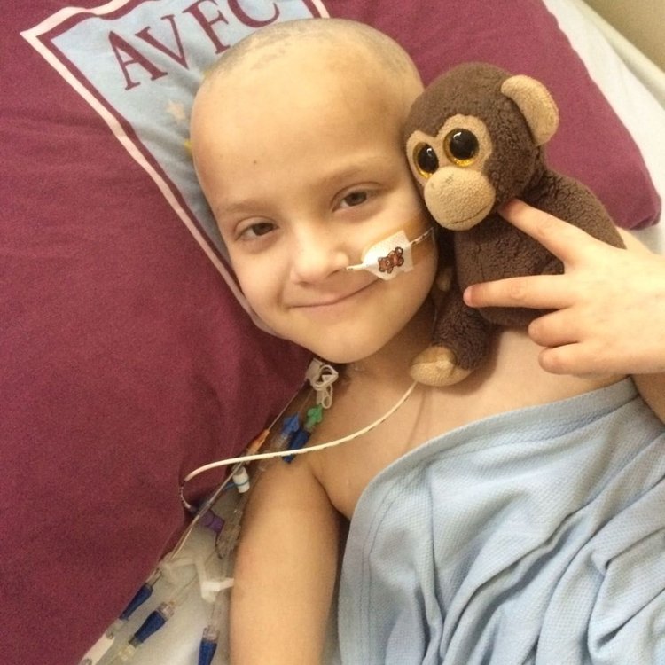 Josh lying down in bed at GOSH. Holding toy monkey and smiling to camera.
