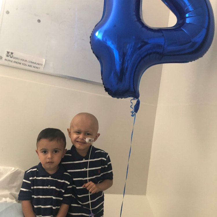 Two boys standing together, one holding a number four balloon.