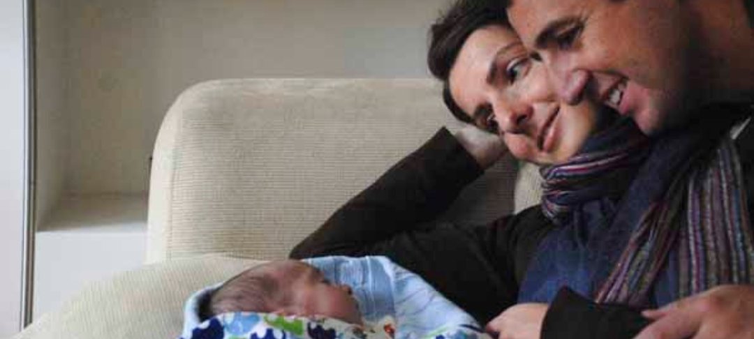 A man and woman hold and smile at their baby boy