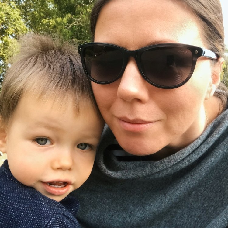 A woman in sunglasses holds her toddler. They're both smiling.