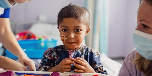Yumna is playing with some brightly coloured shapes. She looks at the camera and smiles.
