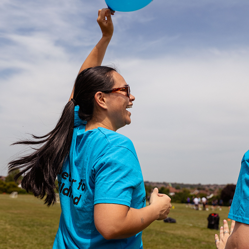 Two women in GOSH Charity t-shirts smile and walk through park holding GOSH Charity balloon