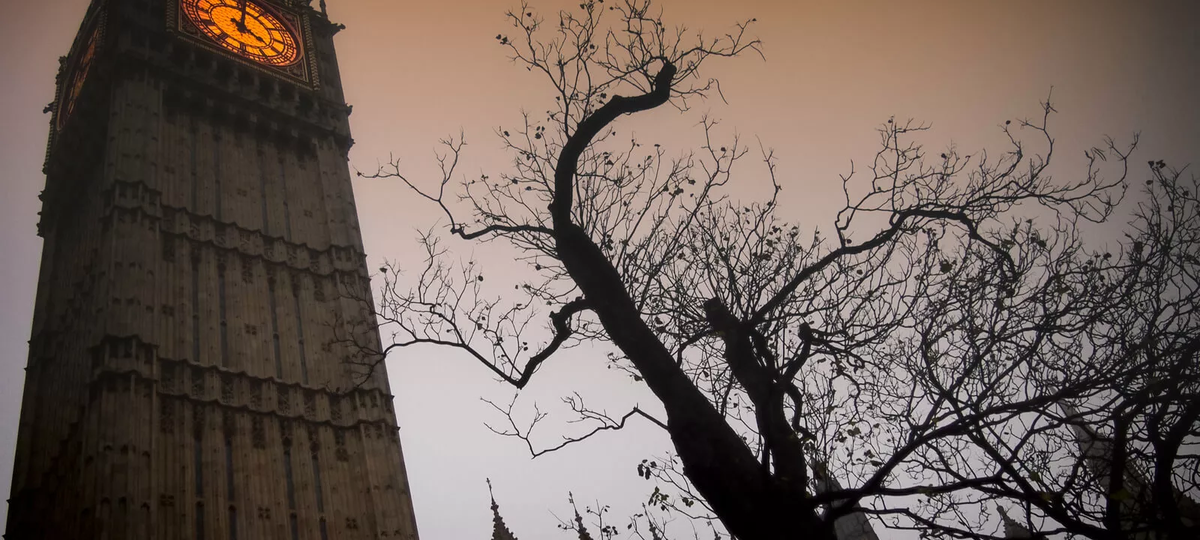 Big Ben at twilight with an orange clock face and the silhouette of a spooky bare tree