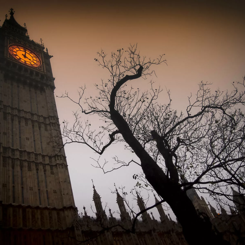 Big Ben at twilight with an orange clock face and the silhouette of a spooky bare tree