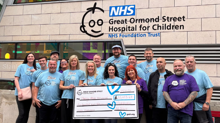A group of people stand outside GOSH holding a giant cheque