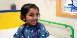 Little girl with feeding tube sitting on bed and smiling