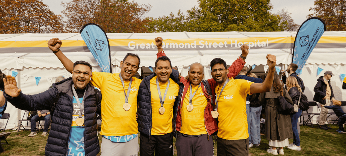 Five runners standing in front of the GOSH Charity Marquee in the Royal Parks Half Marathon event village with their arms in the air, smiling.