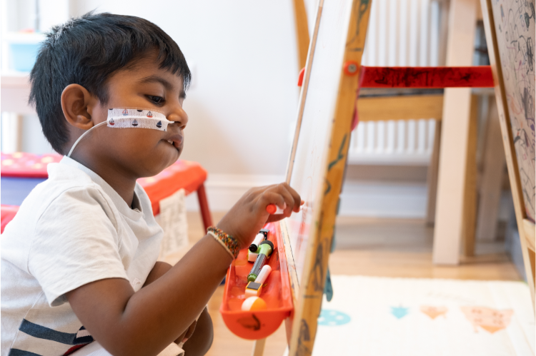 A little boy draws pictures on an easel.